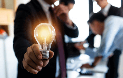 photo of a man holding a lit light bulb with a meeting in the background