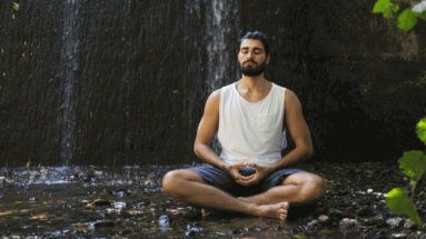 photo of a man meditating next to a small waterfall