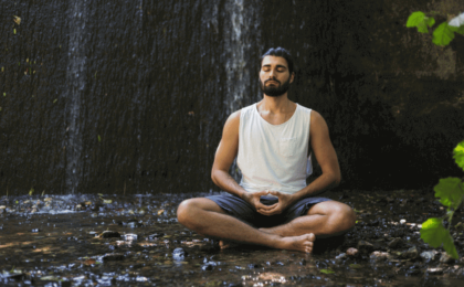 photo of a man meditating next to a small waterfall