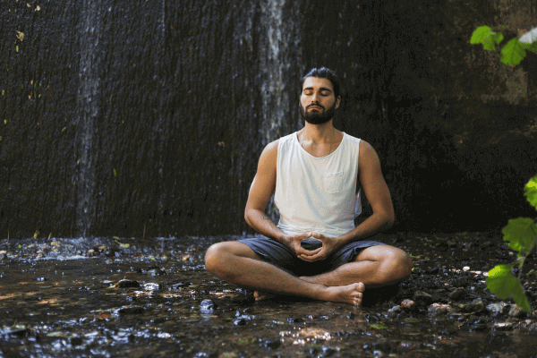 photo of a man meditating next to a small waterfall