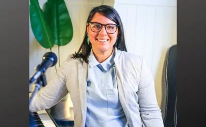 Becky Gilhesbie standing by piano and microphone