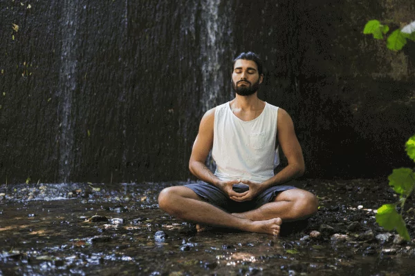 meditate in nature photo of a man meditating next to a small waterfall