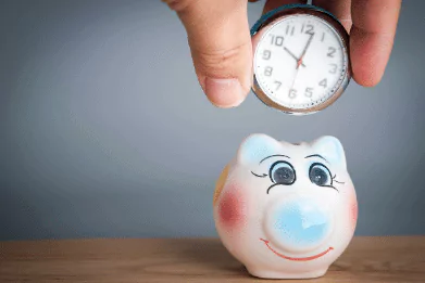 photo of a coin-sized clock being placed into a piggy bank