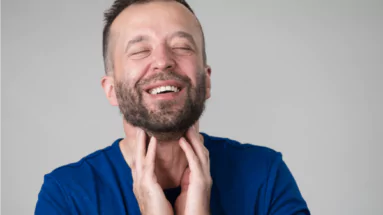 photo of a smiling man with his fingers touching his throat